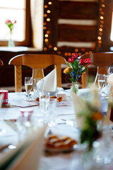 Elegantly set wedding table with flower decorations, champagne glasses, and folded napkins in a cozy wooden interior with warm fairy lights.