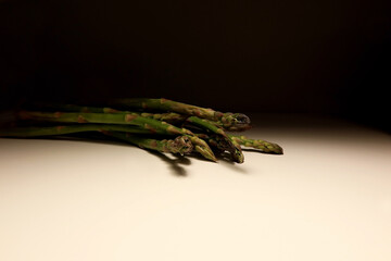 Close-up of a bunch of fresh green asparagus spears on a white surface with dark background....