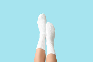 Legs of young woman in white cotton socks on blue background