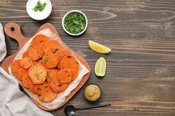 Board with baked sweet potato, sauces, herbs and lemon slices on wooden background