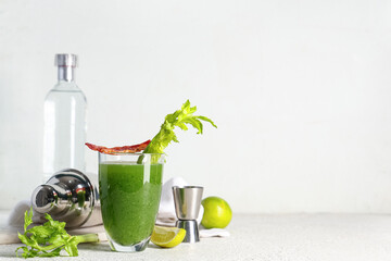 Glass of green bloody mary cocktail with celery, bacon and lime on white background