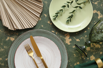 Beautiful table setting with golden cutlery and eucalyptus branches on green background