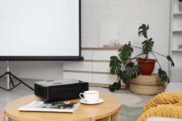 Projector with magazine and cup of coffee on table in room, closeup