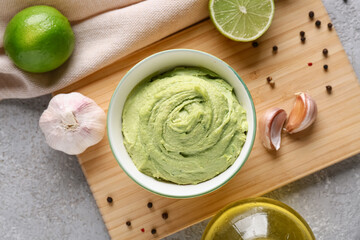 Bowl of tasty peas hummus with lime and garlic on grey background