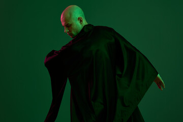A man in a flowing dark robe showcases elegance against a vibrant green backdrop, capturing a...