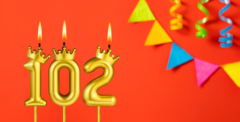 Number 102 birthday candle on an orange background with pennants