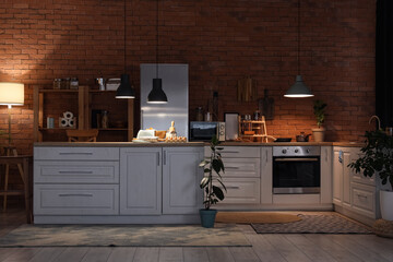 Interior of kitchen with counters, shelf units and glowing lamps at night