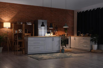 Interior of kitchen with counters, shelf units and glowing lamps at night