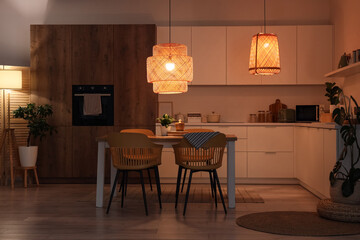 Interior of kitchen with counters, table and glowing lamps at night
