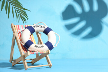 Small deckchair with lifebuoy and palm leaf on color background