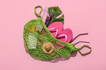 String bag with tropical leaf and beach accessories on pink background