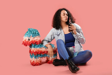 Stylish young African-American woman with soda and pinata blowing kiss on pink background