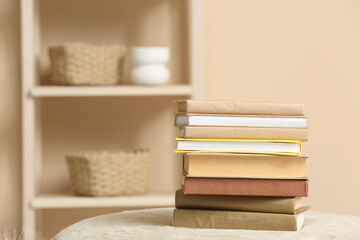 Stack of books on pouf and rack with decor near color wall
