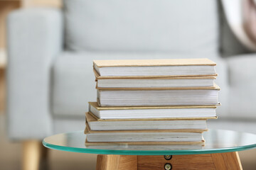 Stack of books on glass table against sofa