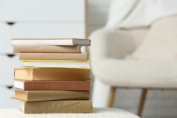 Stack of different books on pouf in light room
