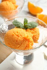 Balls of tasty orange sorbet in dessert bowls, fresh fruit and mint on table, closeup