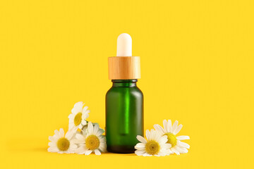 Bottle of chamomile cosmetic oil and flowers on yellow background