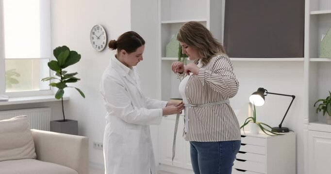 Weight loss. Nutritionist measuring happy overweight woman's waist with tape in clinic