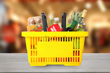 Yellow shopping basket full of groceries on wooden table in supermarket