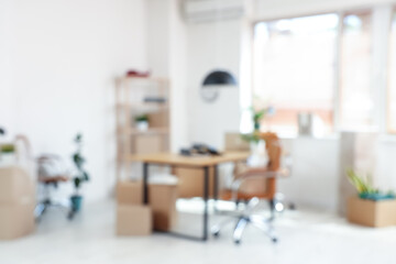 Blurred view of office with workplace, plants and cardboard boxes on moving day