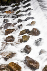 Long-exposure capture of rocks in a rushing stream, highlighting the silky flow of water contrasting the firm stillness of the stones – a symbol of nature's serene strength