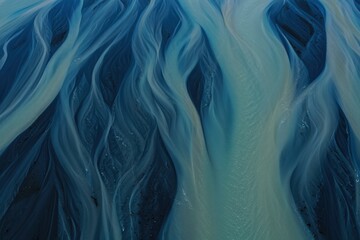 Aerial view of winding river channels flowing through dark terrain creating patterns resembling veins with blue and teal hues