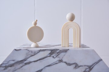Minimalist abstract geometric sculptures consisting of stacked round and semi-circular shapes displayed on a marble surface against a plain light background