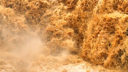 Bird’s eye shot captures powerful sediment-laden floodwaters rushing through rocky terrain,...