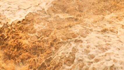 Overhead perspective shows sediment-heavy floodwaters roaring over rocks, emphasizing the growing...