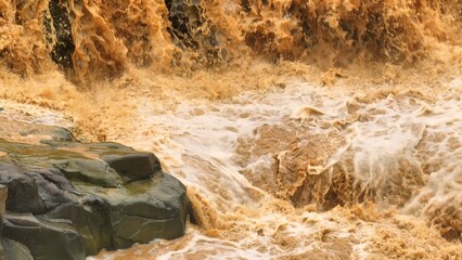Drone aerial view shows muddy floodwaters cascading forcefully, illustrating the intensified flood events linked to climate change and global warming affecting ecosystems and communities. Thailand.
