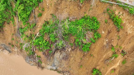 Drone aerial view shows a landslide on a forested slope beside a muddy river, illustrating how extreme weather and climate change increase soil erosion and slope failures in vulnerable areas.