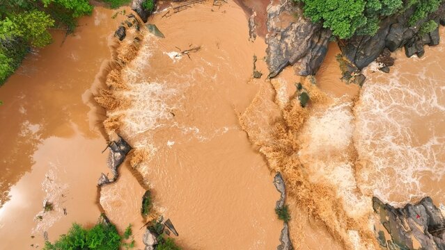 Overhead perspective reveals powerful sediment-laden floodwaters, showing how global warming accelerates extreme weather events and increases flood severity. Thailand.
