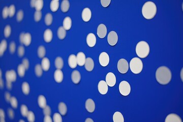 Close-up of scattered white circular discs placed randomly on a bright blue surface creating a pattern with depth of field blur