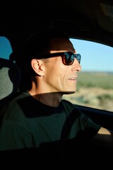 Man wearing sunglasses driving a car in bright sunlight with a calm expression