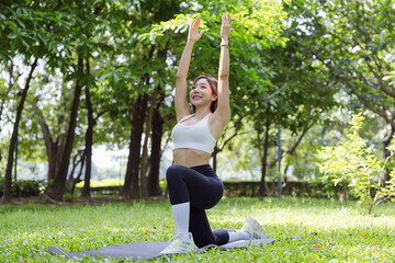 A woman performs a graceful yoga pose in a tranquil park setting, surrounded by lush greenery,...