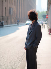 Portrait of handsome Chinese young man wearing gray suit looking back in the street, young guy with black curly hair with urban background. Male fashion, cool Asian young man lifestyle.