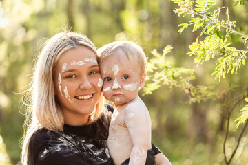 Portrait of mum and baby boy with faces painted in ochre in Australian bushland