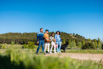 Family walking through a park, carrying picnic baskets and accompanied by their dog, on a beautiful sunny day