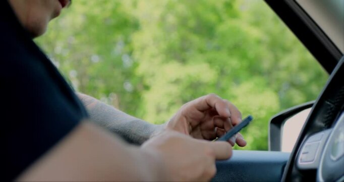 Man using smartphone while seated comfortably inside a car. A person using mobile phone to check email for work or text SMS messages. Online business communication concept. Slow-motion.