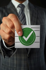 Businessman in suit holds card with green checkmark, symbolizing approval or success. image conveys professionalism and confidence, ideal for business related themes