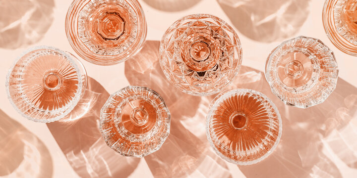 Stylish banner of rose wine crystal glasses casting shadows on pastel peach background. Minimal Top view sparkling alcohol drinking, champagne drinks at sun, wine aesthetic party concept