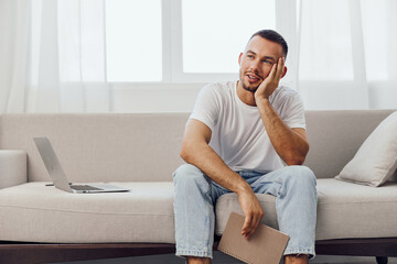 Thoughtful man sitting on a couch while holding a notebook, expressing creativity and inspiration...
