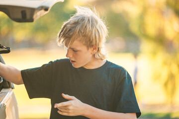 Teenage boy with messy blonde hair standing at back of vehicle on the street © Caseyjadew