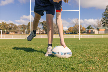 Junior rugby union player reaching down to pick up ball off the field