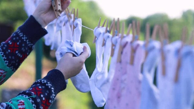 Hands hanging striped baby clothes on a clothesline outdoors on a sunny day &ndash; eco-friendly lifestyle and simple living