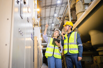 Two engineers in safety vests and helmets inspect electric grid field using tablet and radio near...