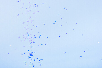 Blue glittering confetti on blue background, top view