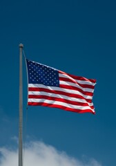 Fototapeta premium American Flag Waving Proudly on a Sunny Day - A vibrant American flag billows in the wind against a clear blue sky, symbolizing patriotism, freedom, unity, strength, and national pride