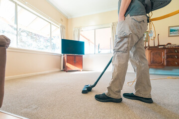 Professional man vacuuming carpet in home in preparation for steam cleaning