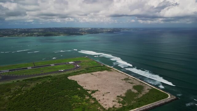 An airplane makes a smooth landing at Bali Airport during daylight hours with views of the runway, nearby ocean, and surrounding tropical landscape.